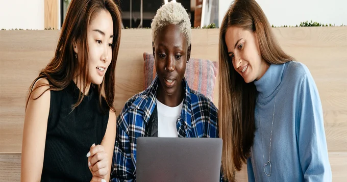 Three women staring at a laptop screen.