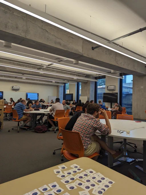 A room full of people brainstorming at separate tables. Civic Tech Toronto stickers are on table in the foreground. 