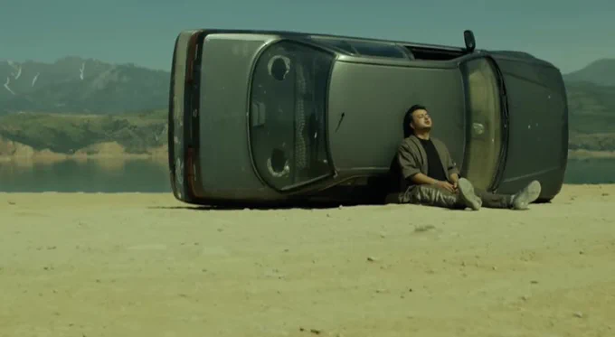 Uzbek rapper Konsta leaning against a turned over car in a mountainous area of Uzbekistan