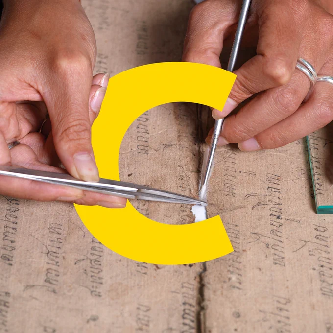 A pair of hands holding tools are treating a tear in a manuscript. The letter C overlaps the hands.