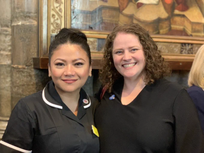 May Parsons, in a black nurse’s uniform, next to Eloise. Both are smiling and looking at the camera.