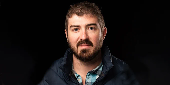 Photo of Travis Weiland, man with brown hair wearing navy jacket and blue plaid shirt