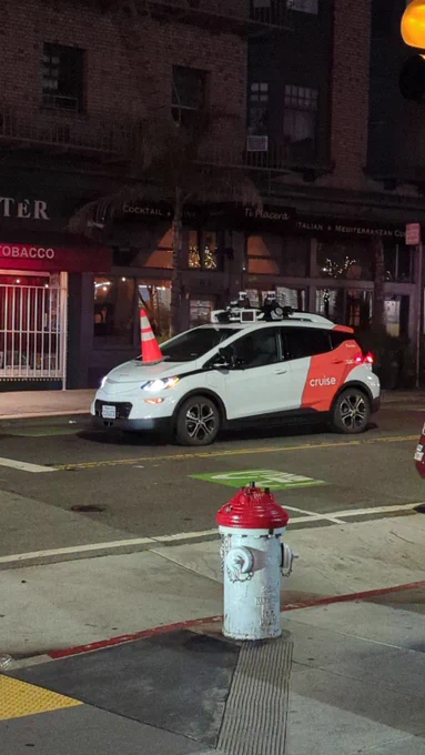 Self-driving cruise car with a cone on its hood at night