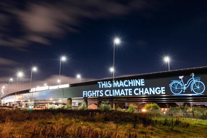 Projection on the side of a road bridge in Glasgow. Picture of a bike with the words "This machine fights climate change".