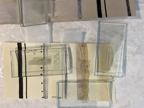 A sheet of paper lies on a piece of Tyvek with different types of stains: tea, coffee, biro pen, ink, permanent marker and Evacon adhesive. Different gels are being tested on each of these stains, some with a barrier layer of Bondina some without, some with a glass weight on top and some without.