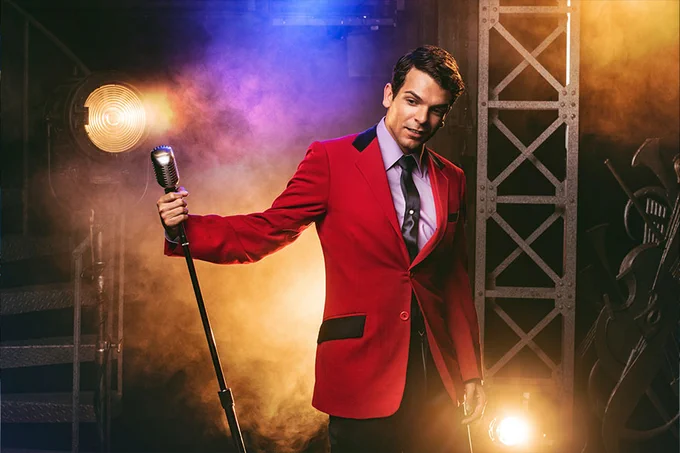 A photo showing a man in a red blazer holding a microphone