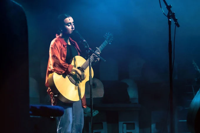 A photo showing a performer holding a guitar on stage