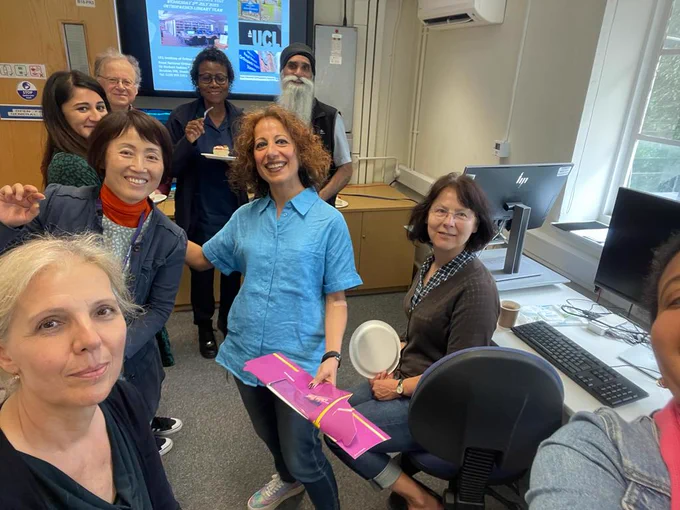 Nine smiling people standing in a room in front of a screen