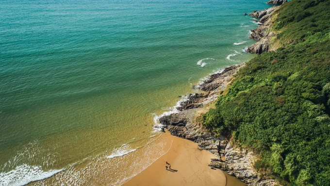 An aerial image of the Welsh coastline on a bright day, where the yellow sand meets the turquoise, clear sea. 