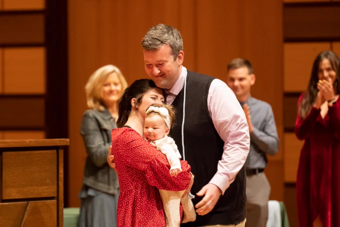 a graduate hugs his wife and child after receiving his cords
