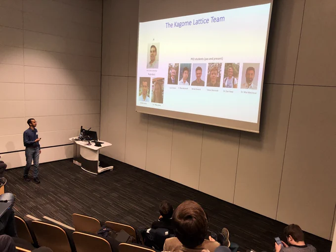 Photo of Mehedi standing at the front of a lecture theatre pointing towards a slide with photos of the kagome team members.