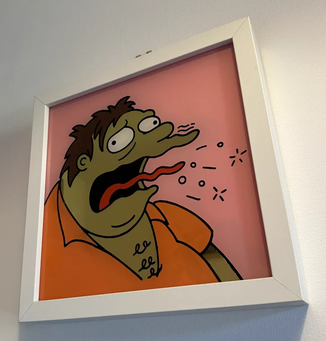 A gold leaf sign of Barney Gumble from The Simpsons burping, with a pink background and white frame