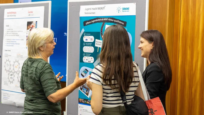 Drei Frauen, die sich vor einem Plakat austauschen.