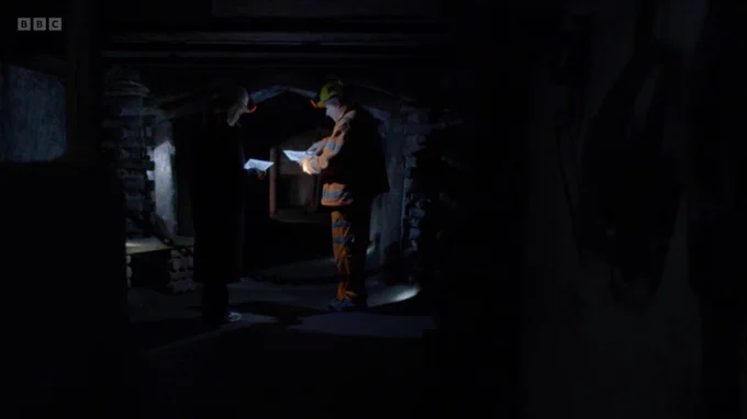 Long shot of Pete and Emily underground looking at documents together