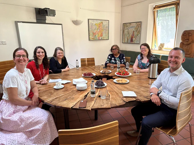 Kiren Collison photographed inside sat around a round table with five members of the Bromley-by-Bow Health Centre Social Prescribing Team. 