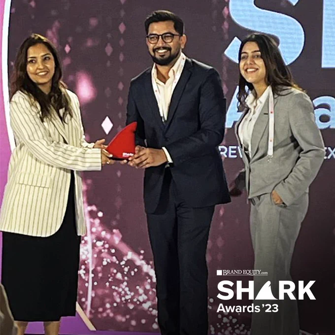 An image of three people standing on stage at the shark awards, accepting an award. the shark awards 23 logo is at the bottom right, with the letter A in shark replaced with a dolphin fin. 