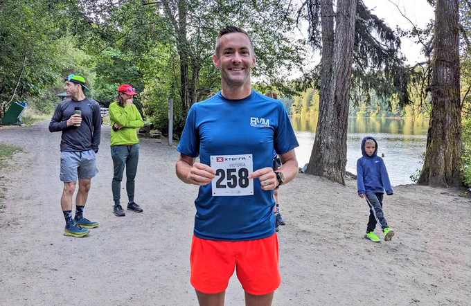 A runner poses with his number, lakeside, smiling widely before the XTERRA Trail Run starts. 