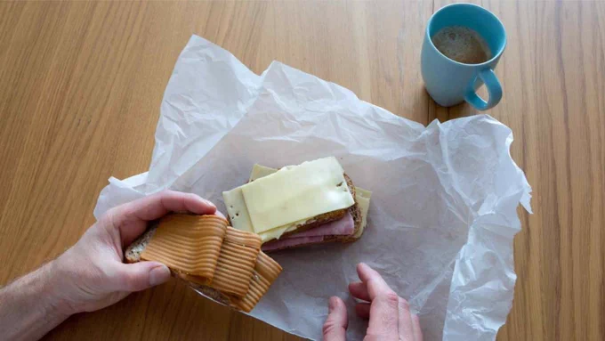 Photo of Norway matpakke from top showing a have on the left holding some ham and a sandwich with cheese on it right next to it. All on top of a white piece of paper.