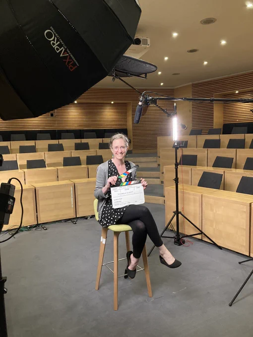Karen sitting on a stool with a clapboard (the thing they snap before starting to film movies) that says “Athabasca”