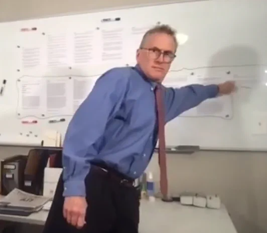 Dave Middlebrook demonstrating text scrolling on a whiteboard in a university classroom with the papers of a journal article pinned to the whiteboard.