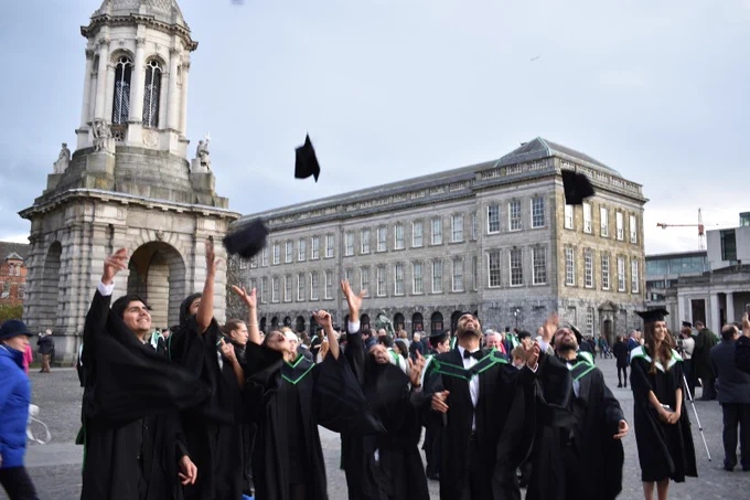 It is graduation day, and a group of proud international students dressed in the traditional gown and cap pose for a photo shoot throw their caps into the air in front of the Campanile.  