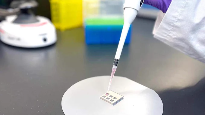 A scientist uses a pipette to place a drop on a square testing device.