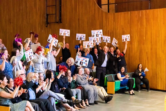 People in an audience holding signs of congratulations.