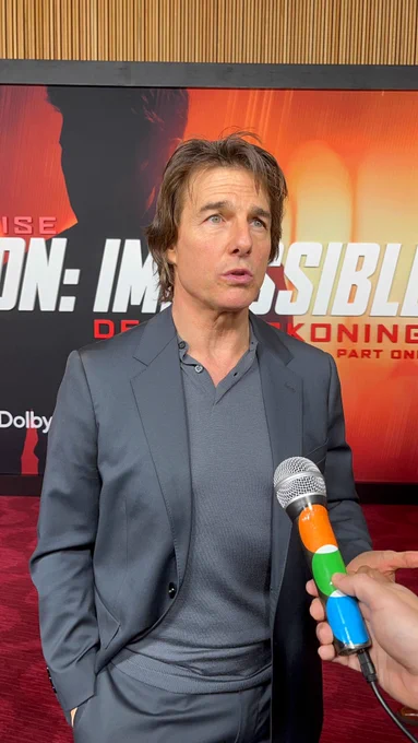 A photo of Tom Cruise on the red carpet for Mission: Impossible – Dead Reckoning speaking into the Letterboxd mic. He is wearing a sharp dark grey suit fit