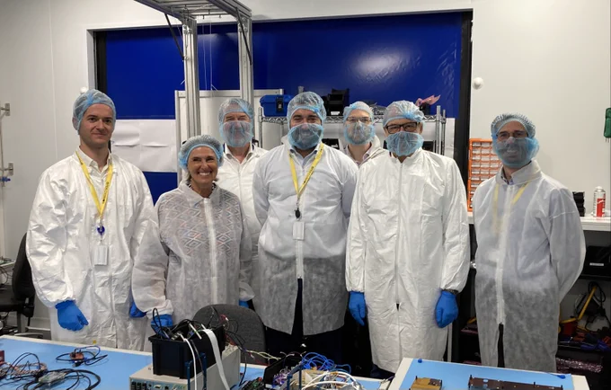 group photo at Open Cosmos facilities with Simonetta Cheli and ESA DG Aschbacher Josef. The group is standing in front of some hardware. 