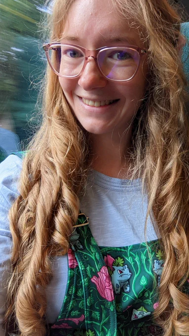 I'm smiling in a train where a forested background is blurring past. I'm wearing a bulbasaur evolutions pinafore.