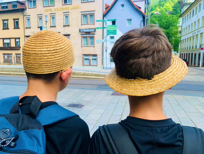 Zwei Jungs von hinten fotografiert. Der eine trägt das Oberteil eines Strohhutes. Der andere die Krempe.