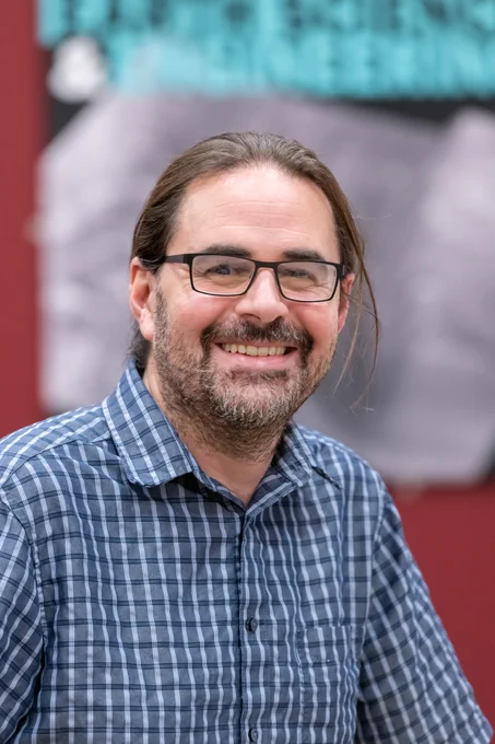 Photo of Mark in blue and white shirt smiling.