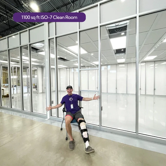 Image of Travis Base standing in front of the clean room with a smile and hands open. Text says ISO 7 Cleanroom