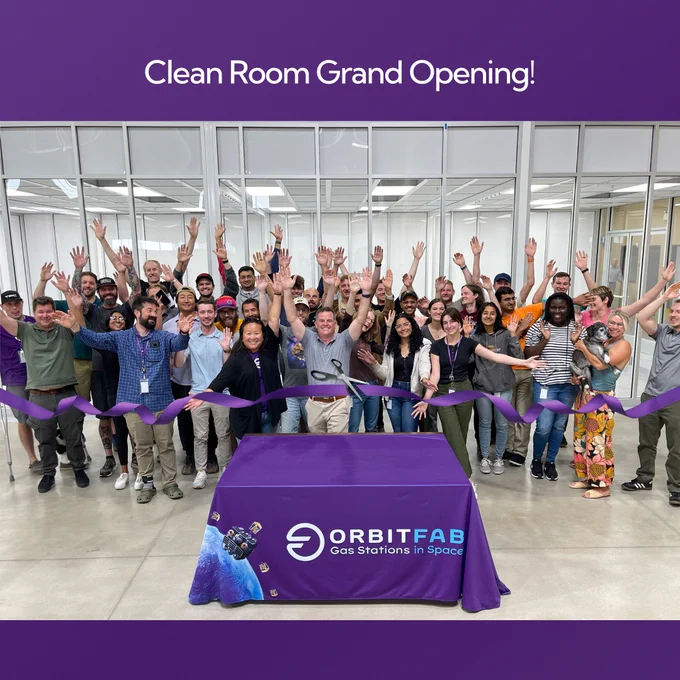 Clean room grand opening. Photo of many people in front of a large clean room and purple ribbon and table with orbit fab logo on it.