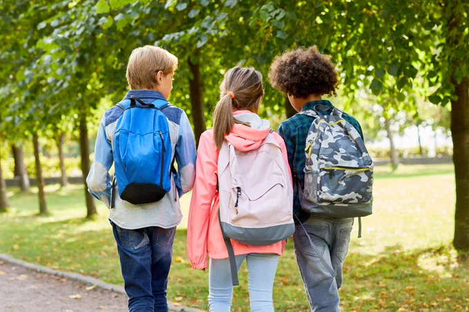 Three students wearing their backpacks outside.