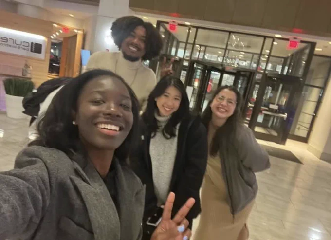 A selfie photo of four smiling people standing in a hotel lobby