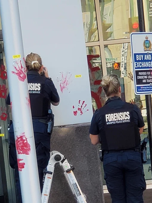 Photo of two cops with forensics vests taking photos of red hand prints on the outside of police HQ