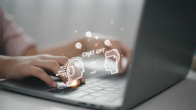 Two hands typing on a grey laptop.  The words "Chat GPT" pop up between the hands.