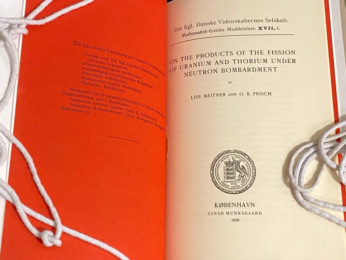 Photo of 1939 publication by Lise Meitner and O.R. Frisch about nuclear fission (from the series Mathematisk-fysiske Meddelelser  XVII, 5). The work is shown open to title page, with red covering to the left.)