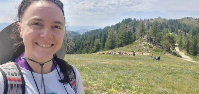 A smiling selfie in front of a subalpine meadow at Bogus Basin in Idaho. In the distance, other botanists closely examine the flora.