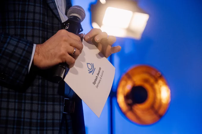 Image is showing the splash award ceremony in Hamburg on November 10th, 2022. The moderator is holding up a card with the Splash Awards logo on its backside.