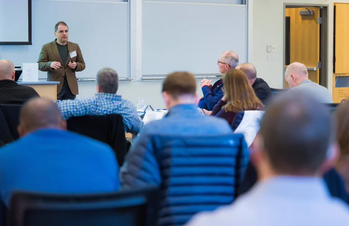 Aleksander Madry stands in front of a whiteboard speaking to a classroom full of participants.