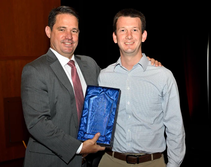 Two adults pose for a picture and smile while holding an award.