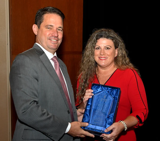 Two adults pose for a picture and smile while holding an award.