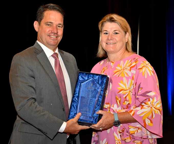 Two adults pose for a picture and smile while holding an award.