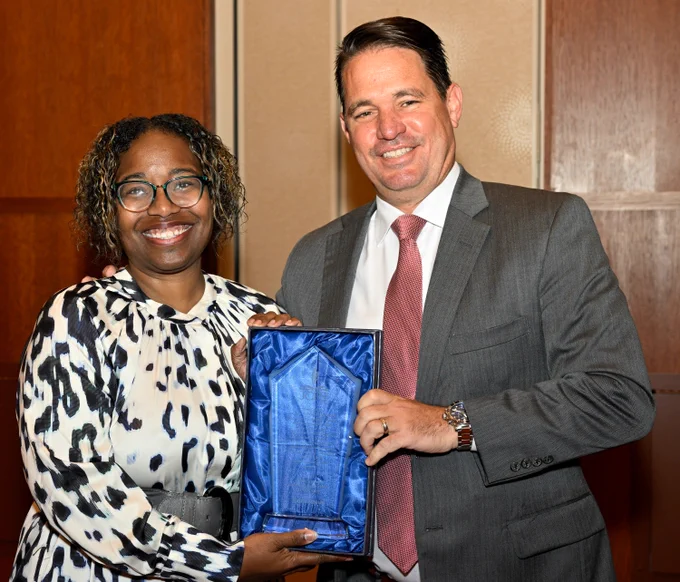 Two adults hold an award and smile.