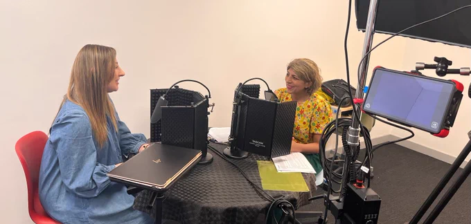 Dr Amy Harrison & Prof Khalida Ismail are sat in a recording studio. They are smiling and speaking into microphones.
