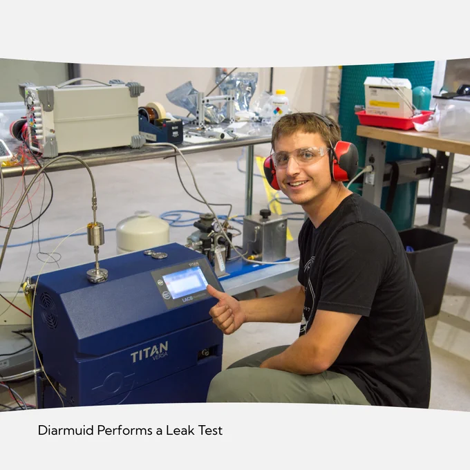 Picture of Diarmuid leaning beside a helium leak detector performing a leak test