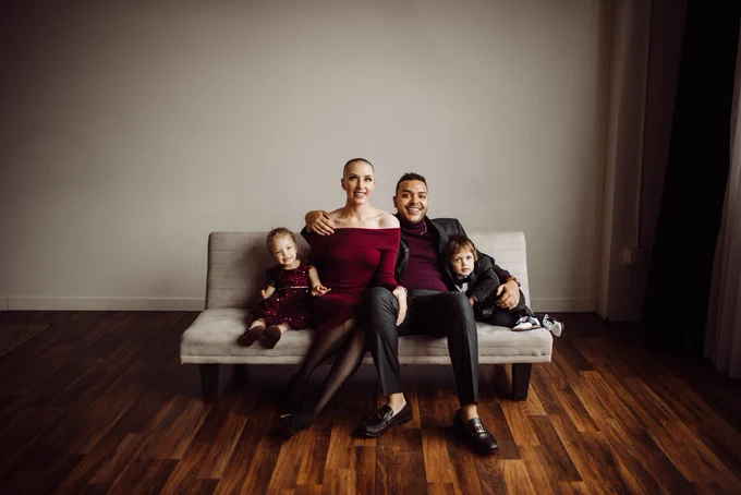 My family all together on a white couch. From left to right. My daughter Sojourner in a red dress, my wife Kathryn in a red dress, myself in a grey suit, my son Stokely in a grey suit.