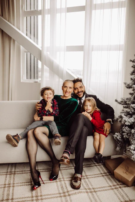 My family all together on a white couch. From left to right. My son Stokely in a red flannel, my wife Kathryn in a green dress, myself in a grey suit, and my daughter Sojourner in a red dress.